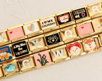 May include: A gold-tone modular link bracelet featuring various decorative charms, including letters, hearts, a spider, flowers, a dog, and text such as I LOVE MY GIRLFRIEND, PEACE, and A BIG KISS FOR MY MOM, with some links containing glittery accents.