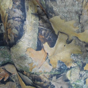May include: Camouflage fabric with a brown, green, and black pattern of leaves and branches.