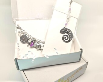May include: A white cardboard box containing a silver charm bracelet and a silver chameleon pendant on a beaded chain. The box lid features the word Dream in gold script with yellow leaf accents. The items are individually packaged in clear plastic.
