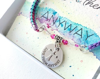 May include: A handmade macrame bracelet in shades of purple, teal, and pink, with a silver charm that reads "Love Them Anyway." The bracelet is displayed on a watercolor card with the word "ANYWAY" and the words "Love them" in the background.