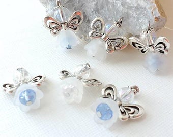 May include: A collection of small, silver-toned angel charms with delicate, openwork wings and clear bead accents. Each angel has a white, flower-shaped body with a light blue center. The charms are displayed on a white surface.