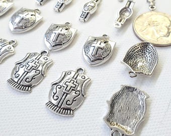 May include: A collection of silver-toned metal charms, including shield-shaped pendants with crosses, watch-shaped charms, and a coin. The charms have a vintage or antique appearance, with intricate detailing and a slightly tarnished finish. Ideal for jewelry making.