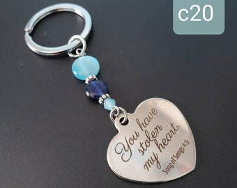 May include: A silver-colored keychain with a heart-shaped pendant. The pendant is engraved with the words "You have stolen my heart" and "Song of Songs 4:9". The keychain features blue and silver beads.
