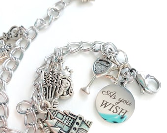 May include: Silver charm bracelet with various charms, including a wine glass, wheat, a crown, and a castle. A round charm is engraved with the words "As you wish". The bracelet has a lobster clasp and an extender chain.