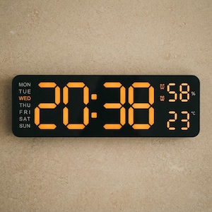 May include: A rectangular black digital wall clock with a bright orange LED display showing the time 20:38, the day of the week as Wednesday, a humidity level of 58%, and a temperature of 23 degrees Celsius, plus two alarm icons.