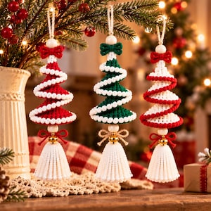 May include: Three hanging Christmas tree ornaments crafted from macrame cord. The ornaments feature spiral designs in red and white, green and white, and white and red. Each piece is topped with a wooden bead and finished with a white tassel.