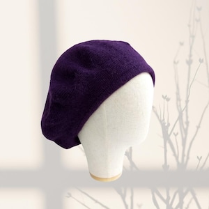 May include: A purple beret made of soft knit fabric. The beret is sitting on a white mannequin head.