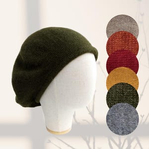May include: A dark green knitted beret on a mannequin head. Next to the beret are circular colour swatches in grey, orange, red, yellow, green, and blue. The beret is a classic style, suitable for various outfits.