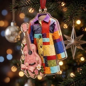 Könnte beinhalten: Ein durchsichtiger Acryl-Weihnachtsbaumschmuck mit einem bunten Patchwork-Mantel mit violettem Kragen und einer rosa Akustikgitarre, die mit weißen Gänseblümchen, einer rosa Schleife und dem in Schreibschrift geschriebenen Namen Dolly verziert ist.