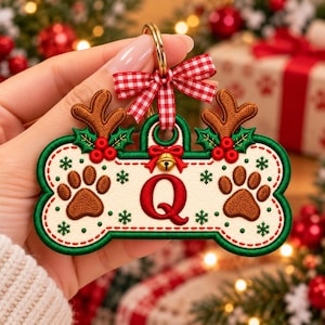May include: A bone-shaped Christmas ornament featuring a cream-colored center with a red letter Q, brown paw prints, and green holly accents. It is topped with a red and white gingham bow, a small gold bell, and brown reindeer antlers.