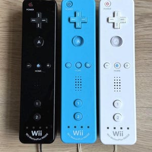 以下が含まれることがあります： 黒、明るい青、白の3つの長方形のビデオゲームコントローラー。各コントローラーには、電源ボタン、十字キー、Aボタン、ホームボタン、プラスボタンとマイナスボタン、スピーカー、1と2のボタンがあります。下部にはWii MotionPlus INSIDEという文字が印刷されています。