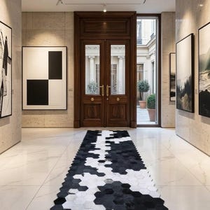 May include: A long runner rug featuring a geometric pattern of black and white hexagonal tiles. The rug is positioned on a white marble floor in a hallway leading to a dark wood double door with glass panels and gold hardware accents.