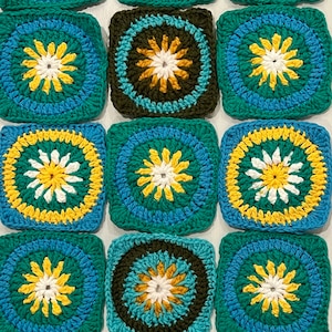 May include: A collection of square crochet pieces in shades of teal, blue, yellow, white, and brown. Each square features a central floral design surrounded by concentric circles. The squares are arranged in a grid pattern, showcasing the handmade texture.