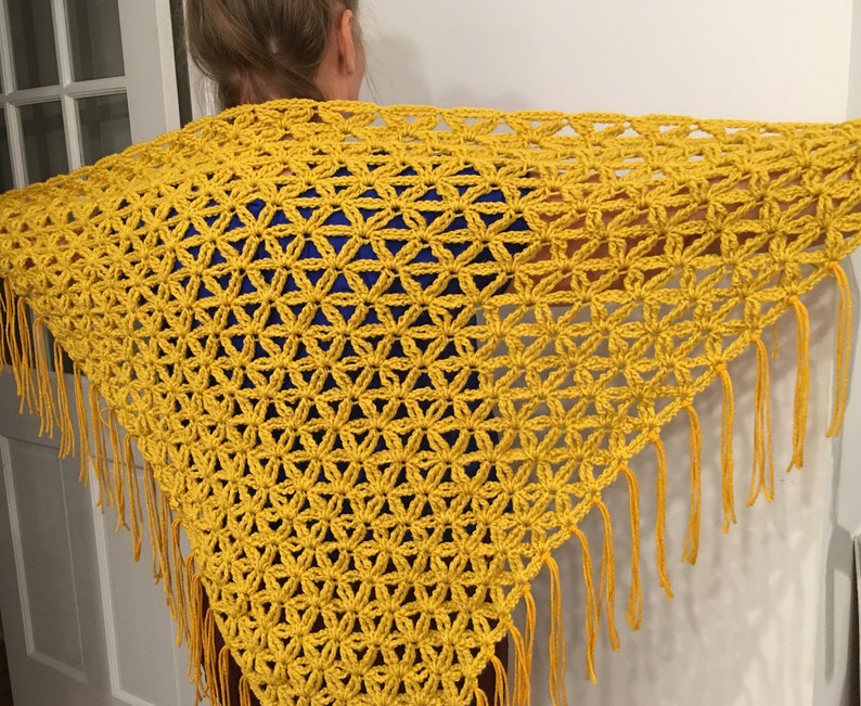 Pu&ograve; includere: Uno scialle di uncinetto giallo con un bordo a frangia. Lo scialle &egrave; realizzato con un delicato punto a maglia che crea un effetto pizzo.