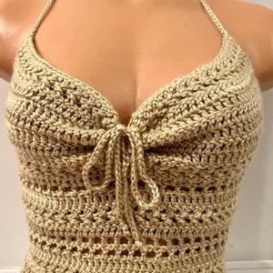 May include: A beige crochet halter top with a tie detail at the front. The top is made with a delicate open stitch pattern.