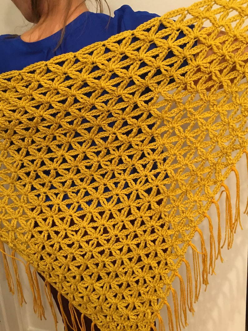 Pu&ograve; includere: Uno scialle all'uncinetto giallo senape con frange. Lo scialle &egrave; realizzato con un delicato punto a maglia che crea un effetto pizzo.