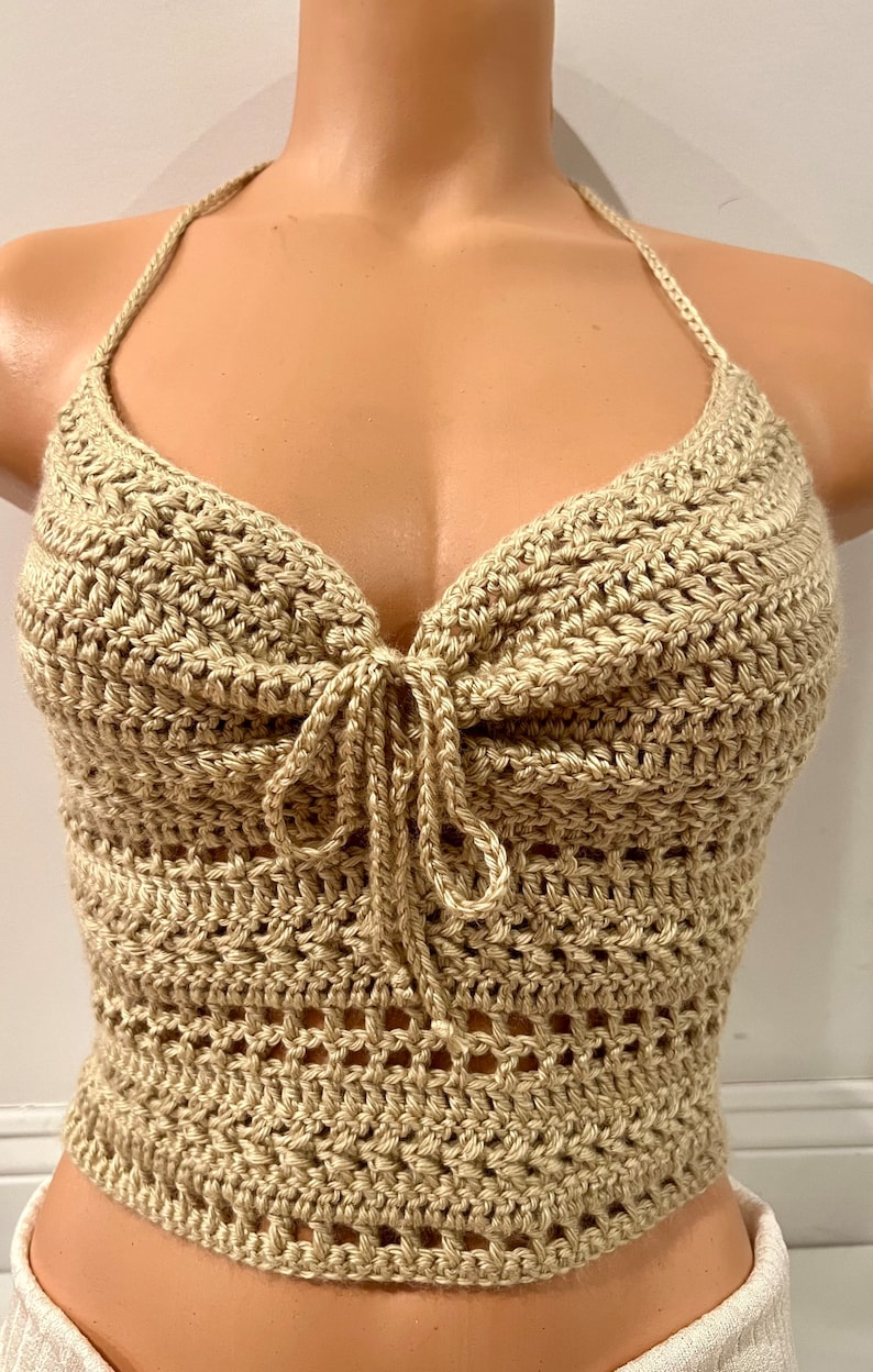 May include: A beige crochet halter top with a tie detail at the front. The top is made with a delicate open stitch pattern.