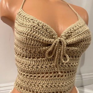 May include: A beige crochet halter top with a tie at the front. The top is made with a delicate open stitch pattern.