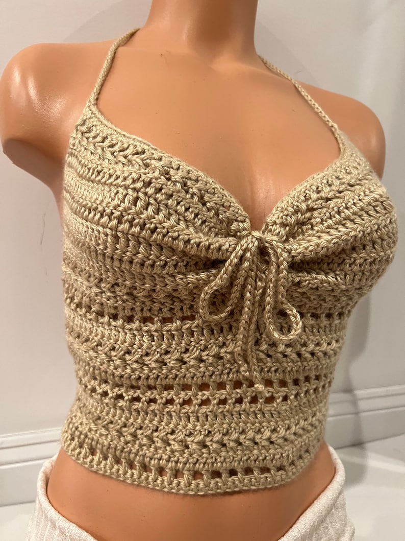 May include: A beige crochet halter top with a tie at the front. The top is made with a delicate open stitch pattern.