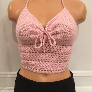 May include: A pink crocheted halter top with a tie at the front. The top is made with a delicate open stitch pattern.