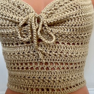 May include: A beige crochet halter top with a tie at the front. The top is made with a delicate open stitch pattern.