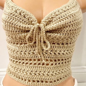May include: A beige crochet top with a tie at the front. The top has a delicate, openwork design.