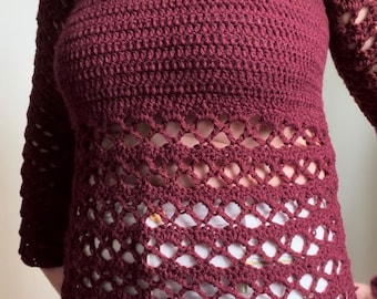 Puede incluir: Un top de ganchillo color granate con un diseño de encaje alrededor de la cintura. El top tiene mangas largas y un escote redondo.
