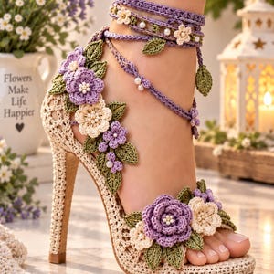 May include: A high-heeled sandal crafted from beige crochet featuring intricate floral embellishments in shades of purple and cream. The design includes green crochet leaves, small white pearl accents, and long ankle-tie straps that wrap around the lower leg.