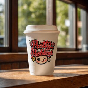 以下が含まれることがあります： 蓋付きの白い紙製使い捨てコーヒーカップ。赤い筆記体で「Pretty Problem」と書かれたグラフィックがプリントされており、その下には舌を出してウィンクしている漫画風の顔と、小さな黄色とピンクの花のアイコンが描かれています。