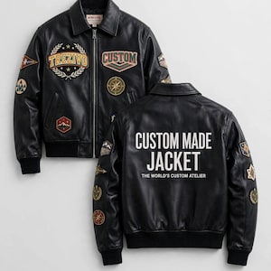 Può includere: Un giubbotto bomber in pelle nera con cerniera frontale, polsini a coste e varie toppe ricamate. La parte anteriore mostra il testo TREZIVO e CUSTOM. Il retro presenta il testo bianco CUSTOM MADE JACKET e THE WORLD'S CUSTOM ATELIER.