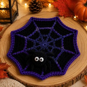 May include: A crocheted black spider web doily with a vibrant purple border and a small, plush black spider attached to the center. The spider features two large, round white eyes with black pupils, creating a distinct contrast against the dark yarn.