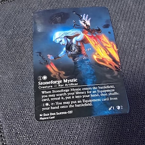 May include: A rectangular trading card featuring a fantasy illustration of a pale figure with long white hair holding two glowing orange blades. The card text reads Stoneforge Mystic, Creature - Kor Artificer, and includes game rules, the artist name Dan Dos Santos-337, and the label Playtest Card.