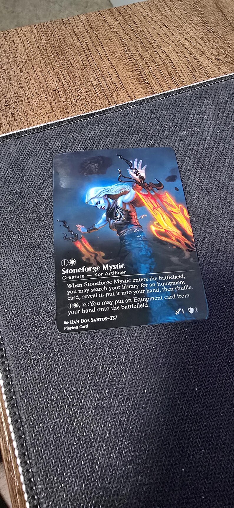 May include: A rectangular trading card featuring a fantasy illustration of a pale figure with long white hair holding two glowing orange blades. The card text reads Stoneforge Mystic, Creature - Kor Artificer, and includes game rules, the artist name Dan Dos Santos-337, and the label Playtest Card.