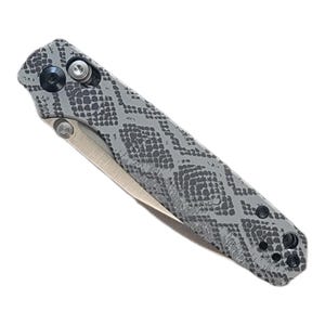 May include: A folding pocket knife featuring a gray handle with a dark gray snakeskin pattern. The knife has a metallic silver blade, a black pivot screw, a silver thumb stud, and a black pocket clip attached to the textured handle surface.