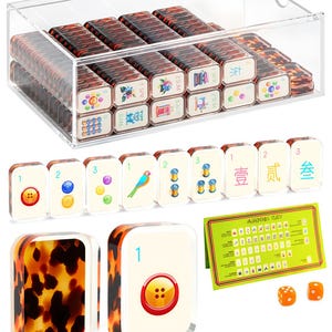 May include: A clear acrylic storage box filled with rectangular mahjong tiles featuring a tortoiseshell pattern on the back and various colorful illustrations on the front. Includes a green instruction card and two orange dice.
