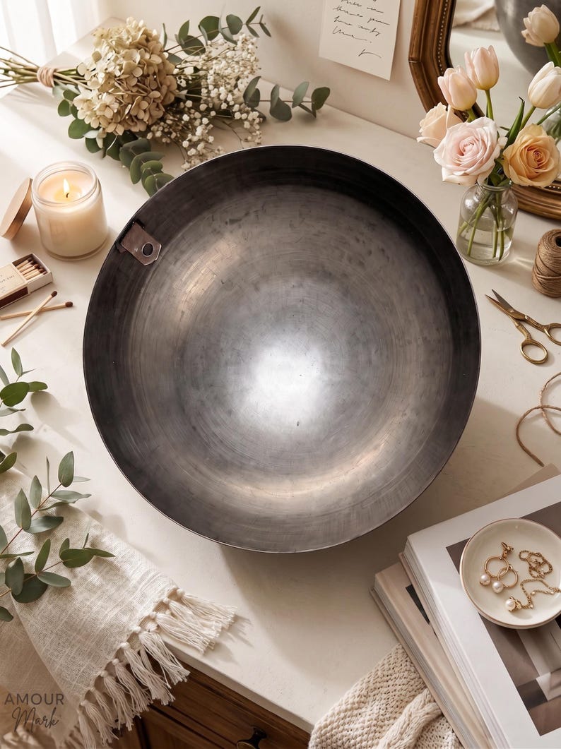 K&ouml;nnte beinhalten: Eine gro&szlig;e, kreisf&ouml;rmige Schale aus dunkelgrauem Metall mit einer glatten, reflektierenden Innenfl&auml;che und einer kleinen Metalllasche am oberen linken Rand. Die Schale hat eine tiefe, beckenartige Form mit einer weiten &Ouml;ffnung.