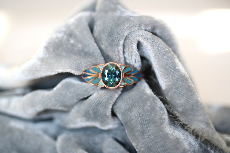 Puede incluir: Un anillo de oro rosa con una piedra ovalada turquesa rodeada de un dise&ntilde;o de esmalte azul y dorado.