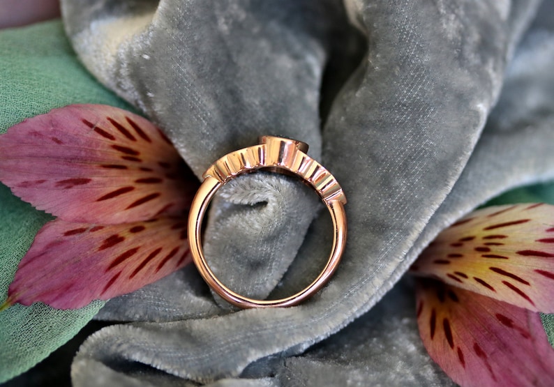 Puede incluir: Un anillo de oro rosa con una banda texturizada y una sola piedra redonda. El anillo se muestra sobre una superficie de terciopelo gris.