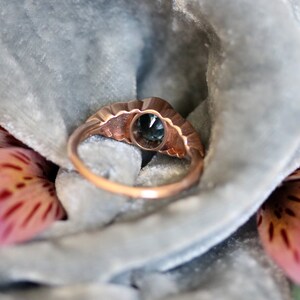 Puede incluir: Un anillo vintage de oro rosa con una piedra ovalada azul engastada en un engaste festoneado. El anillo est&aacute; rodeado de diamantes m&aacute;s peque&ntilde;os.