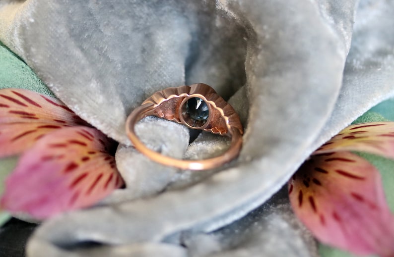 Puede incluir: Un anillo vintage de oro rosa con una piedra ovalada azul engastada en un engaste festoneado. El anillo est&aacute; rodeado de diamantes m&aacute;s peque&ntilde;os.