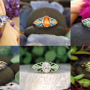 Puede incluir: Seis anillos con piedras preciosas ovaladas engastadas en bandas de oro. Cada anillo presenta un dise&ntilde;o &uacute;nico con acentos de esmalte verde, azul y naranja. Los anillos se muestran en varias superficies, incluidas rocas y tela.