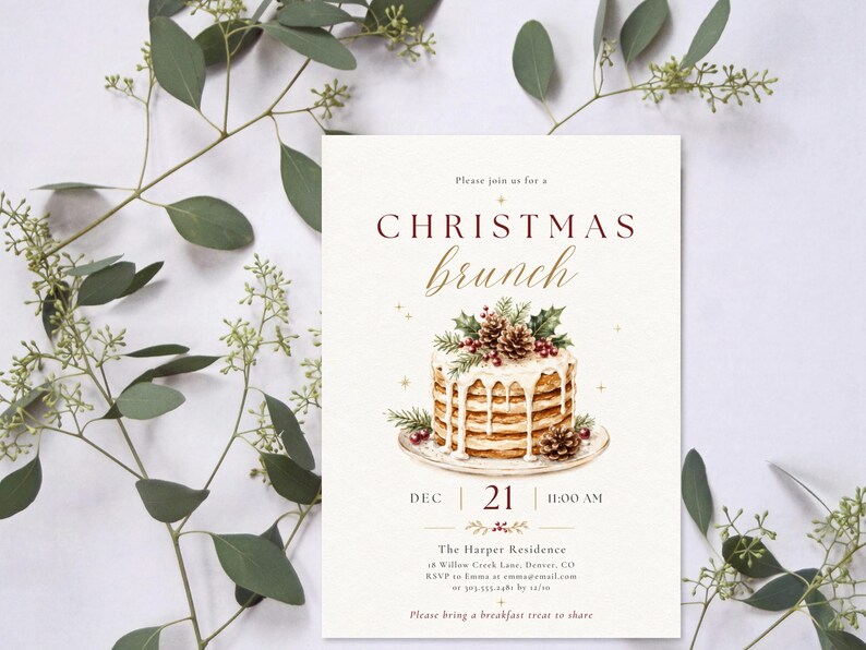 Op de afbeelding: Een rechthoekige uitnodigingskaart met de tekst "CHRISTMAS brunch" in donkerrood en goudkleurig schrift. In het midden staat een aquarelillustratie van een stapel pannenkoeken met wit glazuur, dennentakken en dennenappels op een bord.