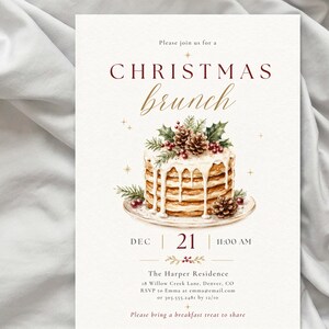 Op de afbeelding: Een uitnodigingskaart voor een kerstbrunch met een aquarelillustratie van een stapel pannenkoeken met wit glazuur, dennenappels en hulst. De tekst luidt: Please join us for a CHRISTMAS brunch, DEC 21, 11:00 AM, The Harper Residence.