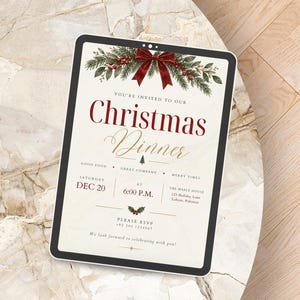 May include: A digital tablet displaying a Christmas dinner invitation with a cream background, red text, and a festive illustration of pine branches, red berries, and a dark red bow at the top. The text includes event details and RSVP information.