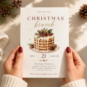 May include: A rectangular Christmas brunch invitation card featuring a stack of pancakes topped with pinecones and holly. The text reads: Please join us for a CHRISTMAS brunch, DEC 21 11:00 AM, The Harper Residence, 18 Willow Creek Lane, Denver, CO.