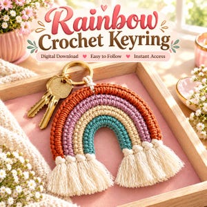 Puede incluir: Un llavero de arcoíris tejido a ganchillo con arcos concéntricos en hilo color naranja quemado, lavanda, crema y verde azulado. La parte inferior del arcoíris termina en flecos color crema. Una anilla de metal dorado sujeta dos llaves de latón.