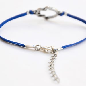 Pu&ograve; includere: Un braccialetto con cordino blu con un ciondolo e una chiusura a forma di cuore color argento. Il braccialetto ha un'estensione a catena per la regolazione delle dimensioni. Il gioiello &egrave; posto su uno sfondo bianco.