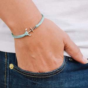 Könnte beinhalten: Ein hellblaues Armband mit einem silbernen Anker-Anhänger. Das Armband wird am Handgelenk getragen.