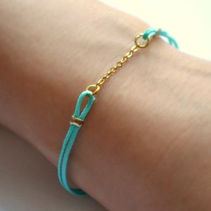 Könnte beinhalten: Ein türkisfarbenes Armband mit einer goldenen Kette, die zwei Schlaufen an beiden Enden verbindet.