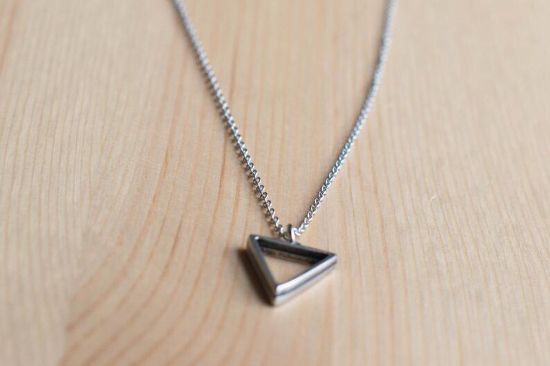 May include: A silver chain necklace with a geometric triangle pendant.